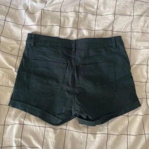 Shorts från H&M, strl 36 - Svarta shorts från H&M i klassisk femficksmodell med uppvikta benslut och bälteshällor. Snygg, enkel design som funkar till många stilar. Materialet är mjuk bomull med lite stretch för extra komfort