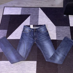 Blå jeans från Nudie Jeans - Snygga blå jeans från Nudie Jeans med klassisk femficksdesign och kontrastsömmar. Jeansen har en rak passform och är tillverkade i slitstarkt denimtyg. Bakfickorna har Nudie Jeans signatursöm och läderpatch med logga bak i midjan.