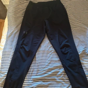 Svarta byxor från Under Armour - Svarta byxor  från Under Armour med diskret logga på benet. Tight passform och elastisk midja, perfekta för träning eller löpning. Tillverkade i ett stretchigt syntetmaterial som andas och ger bra rörelsefrihet.