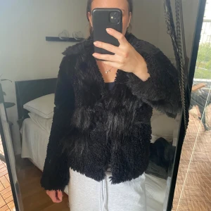 Svart pälsjacka med krage - Säljer en svart pälsjacka med fluffig och mjuk känsla. Jackan har en bred krage och är långärmad, med en cool mix av lockig och slät päls på ytan. Perfekt för dig som vill ha en statement piece i garderoben.
