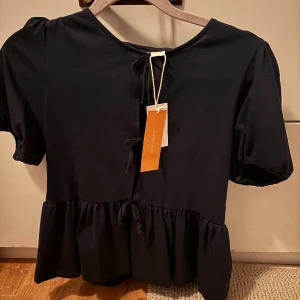 Mörkblå blus med knyt och volang - Supersöt mörkblå blus med korta puffärmar, knyt framtill och volang nertill Från Gina Young💕 aldrig använd och har prislappen kvar i storlek 158-164