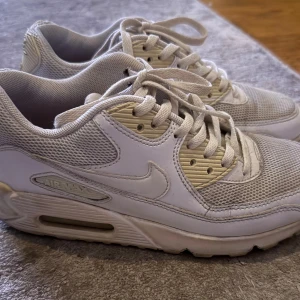 Nike Air Max 90 vita sneakers strl 36.5 - Nike Air Max 90 sneakers i vitt, klassisk mesh och skinnpaneler. Retrodesign med synlig Air Max-dämpning i sulan och snörning framtill. 
