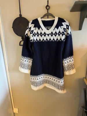 Mörkblå stickad klänning från SHEIN - Mysig mörkblå stickad klänning från SHEIN med vitt och grått nordiskt mönster. Tröjan har v-ringning och långa ärmar med breda muddar. Perfekt för kalla dagar och ger en riktigt vintervibe.