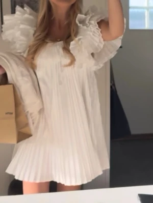 Vit plisserad kortklänning med volang - Säljer nu min superfina vit kortklänning med plisserat tyg och stora volangärmar Jättepopulär och eftertraktad klänning från Zara som är slutsåld, hör av er vid funderingar!