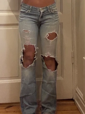 Ljusblå bootcut jeans med hål - Säljer ett par ljusblå jeans med stora slitningar och hål över knäna och låren. 
