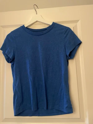 Blå basic t-shirt i bomull - En enkel blå t-shirt med rund hals och korta ärmar. Tillverkad i mjuk bomull som känns skön mot huden. Perfekt till jeans eller shorts för en clean och avslappnad look.