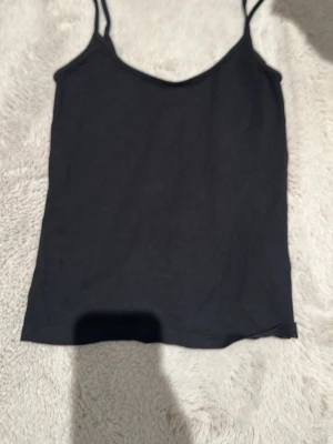 Svart linnetopp från Gina Tricot - En enkel och stilren svart linnetopp från Gina Tricot, basically basics-kollektionen. Toppen har tunna axelband och rak passform, perfekt att matcha med jeans eller kjol. Materialet känns mjukt och lätt mot huden. Från min rensning från garderoben, knappt använd för att den är för den är lite för stor för mig