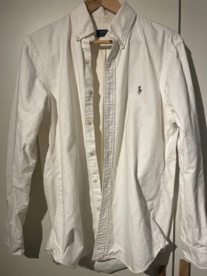 Vit skjorta från Polo Ralph Lauren - Klassisk vit skjorta från Polo Ralph Lauren i bomull med broderad logga på bröstet. Skjortan har lång ärm, knappar hela vägen och button-down-krage.