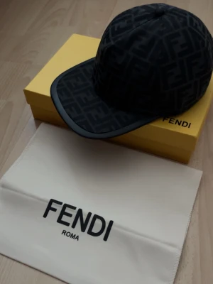 Svart Fendi keps  - Säljer en svart keps från Fendi med det klassiska FF-monogrammet över hela kepsen. Kepsen har böjd skärm och justerbar rem bak. Materialet är mjukt och känns lyxigt, perfekt för dig som vill ha en stilren accessoar med designer-vibe.
