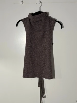 Brun stickad väst med snörning från Zara - Säljer en brun stickad väst med hög krage och snygga snörningsdetaljer i sidorna. Västen är ärmlös och har en loose passform som ger en avslappnad vibe. Perfekt att styla över en skjorta eller t-shirt för en trendig lager-på-lager-look.