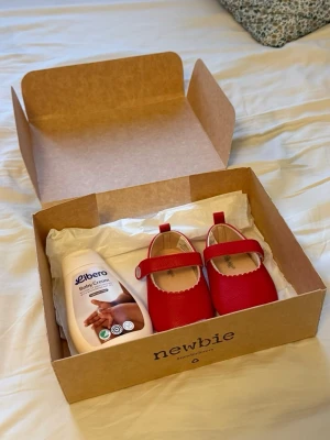 Röda ballerinaskor från Newbie med oanvänd libero Baby Cream  - Supersöta röda ballerinaskor från Newbie för baby eller småbarn. Skorna har rund tå, kardborreband över foten och är gjorda i ett mjukt syntetmaterial med lätt struktur. Perfekta för att ge en färgklick till outfiten!