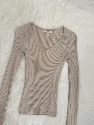 Beige ribbad tröja  - Supersnygg beige ribbad tröja från Amisu med v-ringning och lång ärm. Tröjan har en tight passform och är gjord i mjukt, stretchigt material som sitter riktigt snyggt på kroppen. Perfekt till lager på lager under höst och vår.