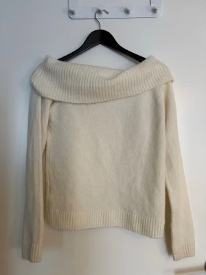 Dan offshoulder stickad tröja  - Superfin offshoulder stickad tröja i vit/krämvit med bred ribbad kant upptill och vid ärmslut i storlek 158/164cm. Perfekt för dig som vill ha en mysig men ändå stilren look. Långärmad och mjuk, passar till allt från jeans till kjol. Är som o nyskick. 