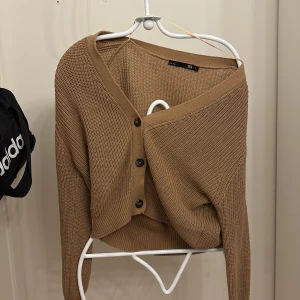 Beige kofta!! - Säljer en beige ribbad kofta i stickad bomull med v-ringning och tre mörka knappar framtill. Koftan har lång ärm och en croppad passform som ger en avslappnad men trendig look. Perfekt att slänga över en topp eller klänning. Storlek S men skulle säga den passar XS bättre!! Skriv om frågor🫶🏼🥰