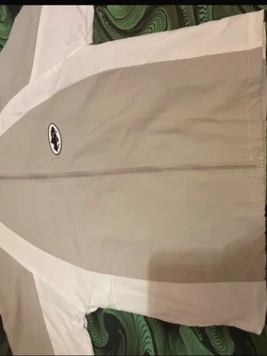 Beige och vit Corteiz vindjacka S - Säljer en beige och vit vindjacka från Corteiz med meshfoder och snygga kontrastpaneler. Jackan har dragkedja framtill, hög krage och logga på bröstet samt broderad text på ryggen. Perfekt för dig som vill ha en clean och sportig look.