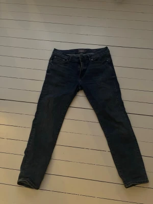 Mörkblå slim fit jeans från Dressmann - Säljer ett par mörkblå slim fit jeans från Dressmann. Klassisk femficksmodell med dragkedja och bälteshällor. Jeansen har en smal passform och är tillverkade i ett mjukt bomullsmaterial med lite stretch för extra komfort.