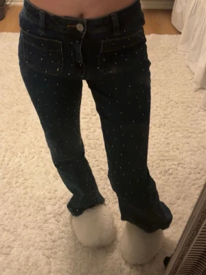 Mörkblåa jeans med diamanter och fickor - mörkblåa jeans som är högmidjade med små diamanter på framsidan och fickor fram och bak. 
