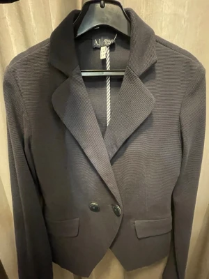 Svart kavaj från Armani Jeans  - Säljer en svart kavaj från Armani Jeans. Kavajen har dubbelknäppning med märkta knappar, klassisk krage och två fickor framtill. Materialet är ribbat och ger en snygg struktur. Perfekt för dig som vill ha en stilren och tidlös look. Säljs i befintligt skick🤗