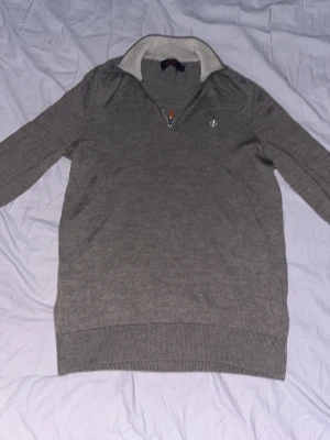 Grå/brun half zip tröja från Morris - Säljer en stilren grå/brun långärmad tröja från Morris med half zip och ribbad krage i ljusare ton. Tröjan har en liten broderad logga på bröstet och är gjord i mjukt stickat material. Perfekt för lager på lager under höst och vinter.