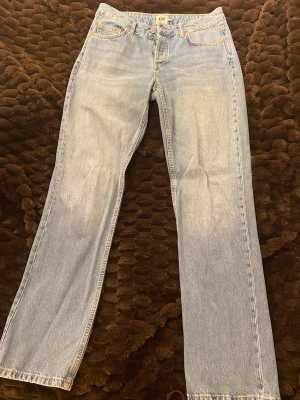 Ljusblå raka jeans från 157, M - Ljusblå jeans från 157 i rak modell med klassisk femficksdesign och knappgylf. Jeansen har kontrastsömmar och är tillverkade i slitstarkt denimtyg. Perfekta för en avslappnad och trendig look.