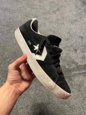 Svarta Converse CONS sneakers mocka - Säljer ett par svarta Converse CONS sneakers i mocka med beige sula och vita detaljer på sidan. Skorna har snörning och klassisk låg profil. Perfekta för dig som gillar streetwear och skate-vibe. Gummisula med bra grepp och diskret gulddetalj vid snörningen.