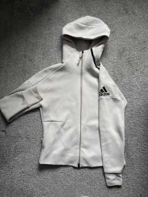 Vit/ljusgrå adidas ziptröja - Säljer en snygg adidaströja med dragkedja i ett grymt material. Passar både kvinnor (storlek M) och män (storlek S). 