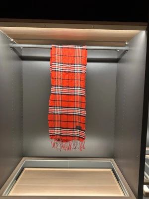 Rutig röd halsduk från Burberrys - Säljer en klassisk röd halsduk från Burberrys i 100% lammull. Halsduken har ett rutigt mönster i svart, vitt och beige samt fransar i kanterna. Perfekt accessoar för att lyfta din outfit med en tidlös brittisk vibe.