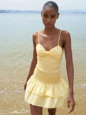 Klänning - Superfin gul kort klänning med tunna axelband, volangkjol och söt rosett i ryggen. Klänningen har ett diskret rutigt mönster och är perfekt för varma dagar. Sitter tajt upptill och har en lätt utsvängd kjol med dubbla volanger. Perfekt för dig som vill ha en söt och fräsch look! Är i storlek L men sitter som m