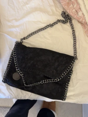 Svart axelväska med kedjedetaljer - Snygg svart axelväska med grov silverfärgad kedja som axelrem och runt kanterna. Jättefin väska men kommer inte till användning längre 