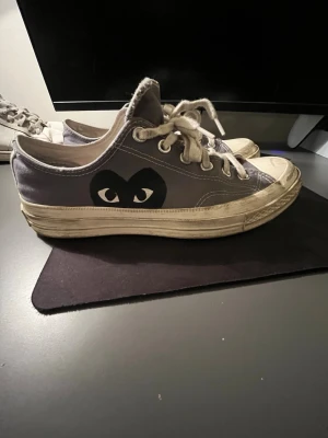 Grå sneakers Comme des Garçons Play - Säljer ett par grå sneakers från Comme des Garçons Play med den ikoniska hjärtloggan på sidan. Skorna har vita snören, vit sula och är tillverkade i canvas. Klassisk låg modell med rund tå och platt sula, perfekta för en streetwear-look.