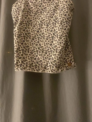 Leopardmönstrad topp från Ü - Säljer en snygg leopardmönstrad topp från Ü i beige och svart. Toppen har en rak passform och är ärmlös, perfekt för dig som vill sticka ut lite extra. Tillverkad i mjuk bomull som känns skön mot huden. Liten metallbricka med logga nertill.