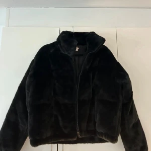 Svart pälsjacka med dragkedja - Mysig svart pälsjacka med hög krage och dragkedja framtill. Jackan har en oversized passform. Storlek 38/40 från Nelly. Använd fåtal gånger så gott skick. 
