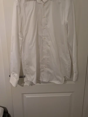 Vit slim fit skjorta Dressmann XL - Klassisk vit skjorta från Dressmann i slim fit-modell. Skjortan har långa ärmar, knappar framtill och är tillverkad i ett skönt bomullsmaterial som är strykfritt. Perfekt för dig som vill ha en clean och stilren look.