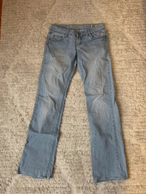 Ljusblå jeansbyxor med broderade fickor - Säljer ett par ljusblå jeansbyxor från M.K. Jeans i storlek 27. Byxorna har raka ben och snygga broderade detaljer i gult på bakfickorna. Klassisk femficksmodell med normal passform och bälteshällor.