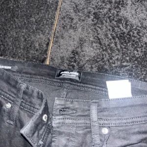 Svarta jeans från Jack & Jones - Säljer ett par svarta jeans från Jack & Jones. Klassisk femficksmodell med raka ben och normal passform. Jeansen har bälteshällor, knappgylf och är tillverkade i ett mjukt bomullsmaterial med lite stretch för extra komfort.