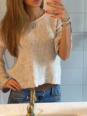 Beige stickad tröja med lös passform - Säljer en beige stickad tröja med avslappnad, boxig passform och rund hals. Tröjan har långa ärmar och ribbade muddar vid ärmslut och nederkant. Perfekt att slänga på sig till ett par jeans för en chill look.