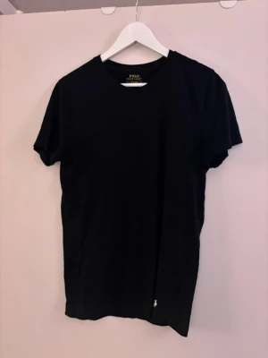 Svart t-shirt Polo Ralph Lauren - Klassisk svart t-shirt från Polo Ralph Lauren i modellen Custom Slim Fit. Tillverkad i mjuk bomull med rund hals och korta ärmar. Diskret broderad logga i vitt nedtill på framsidan. Enkel och stilren design som funkar till allt.