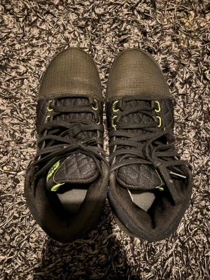 Svarta sneakers med gröna detaljer - Snygga svarta sneakers med mesh och quiltade partier, gröna detaljer på sidorna och snörning. Skorna har en platt sula med transparent grön sektion och rund tå. Perfekta för dig som vill sticka ut med en unik look.