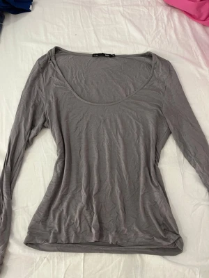 Grå långärmad topp  - En enkel och stilren grå långärmad topp. Toppen har rundad urringning och är tillverkad i ett mjukt och tunt material, perfekt för lager-på-lager eller som den är. Passformen är normal och toppen är lätt att matcha med olika outfits.