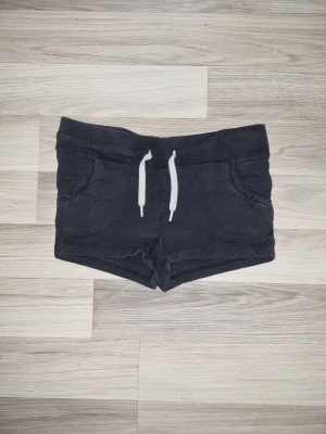 Svarta shorts med snörning - Svarta shorts i mjukt material med vita snören i midjan och två fickor framtill. De har en kort och tight passform, perfekt för varma dagar eller träning. Enkel och stilren design utan mönster.