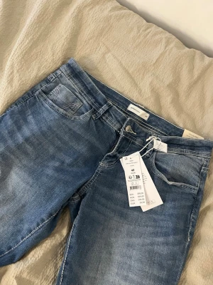 Blå bootcut jeans från Gina Tricot - Säljer ett par blå bootcut jeans från Gina Tricot med klassisk femficksmodell och snygg tvättad look. Jeansen är låg midjade bootcut med lite rosa detaljer längs sömmarna, storlek 40 men passar mindre skulle jag säga, helt nya med prislapp kvar