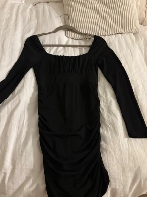 Svart långärmad kort klänning - Snygg svart kort klänning med långa ärmar och rynkade detaljer. Klänningen har en fyrkantig urringning och sitter tight för en smickrande siluett. Perfekt för dig som gillar en enkel men elegant look. Man kan även ha den off-schoulder. Använd 1 gång. Mycket bra kvalitet. Köpt från bikbok.