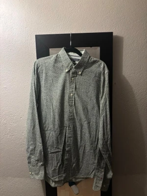 Grön mönstrad skjorta Tommy Hilfiger - Snygg grön skjorta från Tommy Hilfiger med diskret blommigt mönster. Skjortan har klassisk krage, knappar framtill och långa ärmar. Tillverkad i mjuk bomull som känns skön mot huden. Perfekt för dig som vill ha en stilren men ändå unik look.