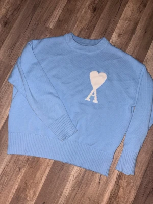 Ljusblå stickad tröja från Ami - Säljer en ljusblå stickad tröja från Ami Alexandre Mattiussi med ikoniskt hjärta och A på bröstet. Tröjan har rund hals, ribbade muddar och är långärmad. Perfekt för dig som vill ha en clean men ändå statement look.