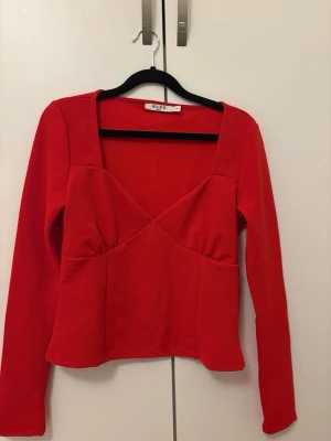 Röd långärmad topp från NA-KD - Trendig röd topp från NA-KD med lång ärm och snygg v-ringad skärning framtill. Toppen har en figurnära passform och är tillverkad i ett stretchigt material som ger en bekväm känsla. Perfekt att styla med jeans eller kjol. Använd endast 2 gånger.