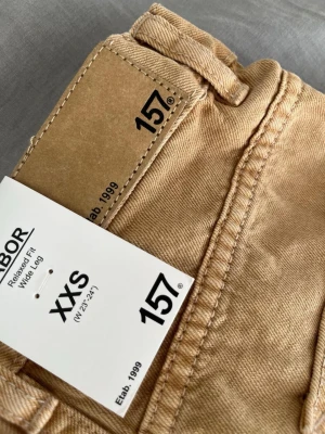 Beige wide leg jeans från 157 - Säljer ett par beige wide leg jeans från 157 i storlek XXS. Byxorna har relaxed fit, stora fickor fram och bak samt en snygg, enkel design. Perfekta för dig som gillar en avslappnad och trendig look.