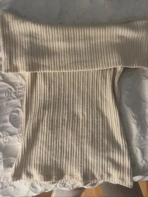 Ribbad offshoulder topp i beige - Trendig ribbad offshoulder topp i beige med croppad passform. Perfekt att styla med jeans eller kjol för en snygg look. Mjuk och stretchig, sitter bekvämt och framhäver axlarna.