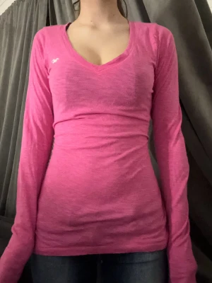 Rosa långärmad topp Hollister - Säljer en rosa långärmad topp från Hollister med v-ringning och figurnära passform. Toppen har en liten vit logga på bröstet 