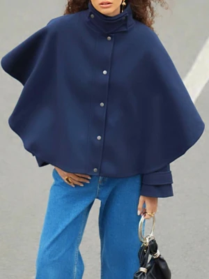 Mörkblå cape-kappa med knappar - Stilren mörkblå cape-kappa med hög krage och knäppning framtill. Kappan har en vid, svepande siluett och är tillverkad i ett tjockare material som passar perfekt för kyligare dagar. Snygg detalj med manschetter vid ärmsluten och minimalistisk design.