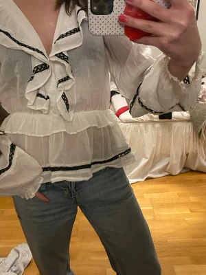 Vit volangblus med svarta detaljer - Säljer en superfin vit blus med volanger och svarta detaljer❤️❤️pris kan diskuteras 